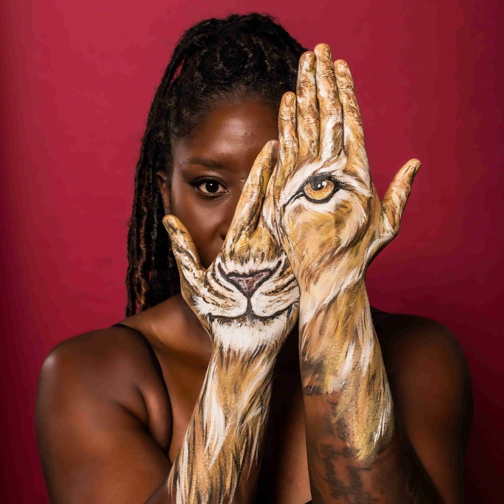 Anita with two painted hands to her face to look like a lioness